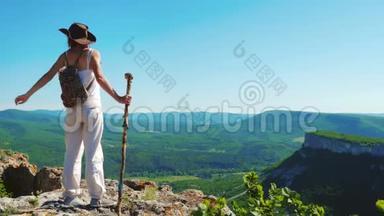穿着牛仔帽和白色衣服的女旅行者<strong>站在山顶</strong>上，欣赏着令人惊叹的景色。